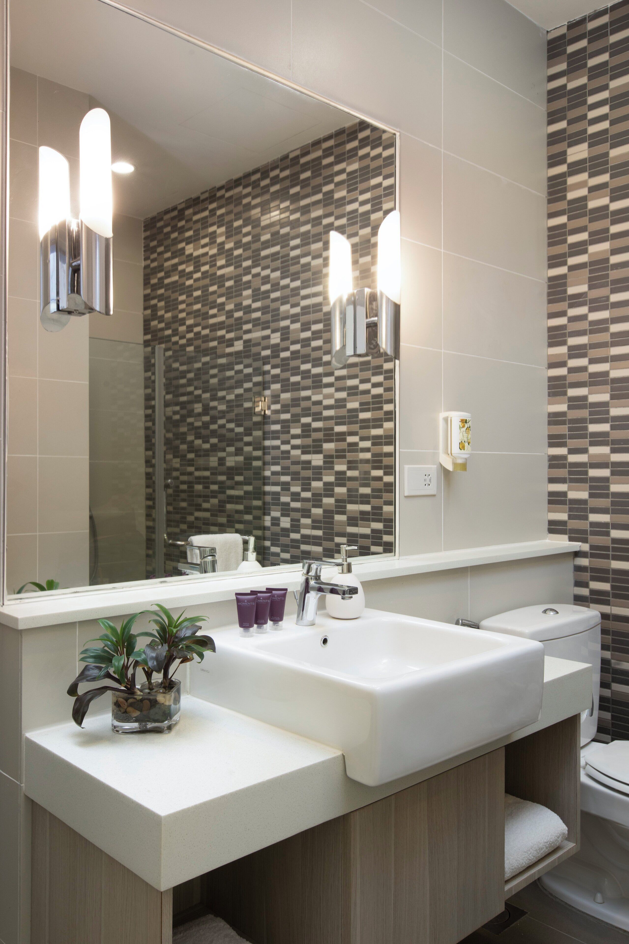 A modern bathroom with a large mirror, two sinks, a toilet, and a tiled backsplash.