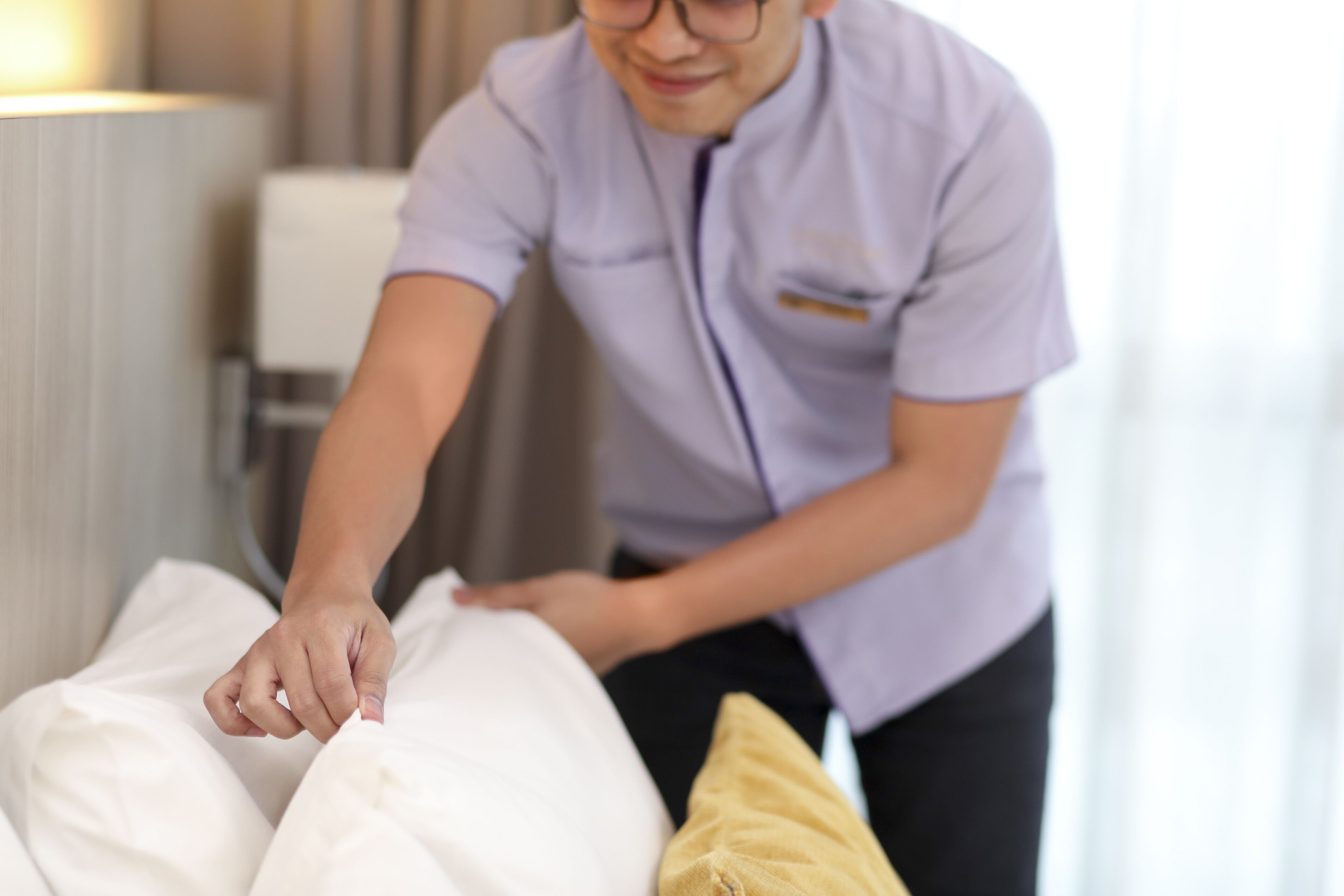 A person adjusting a bed in a hotel room.