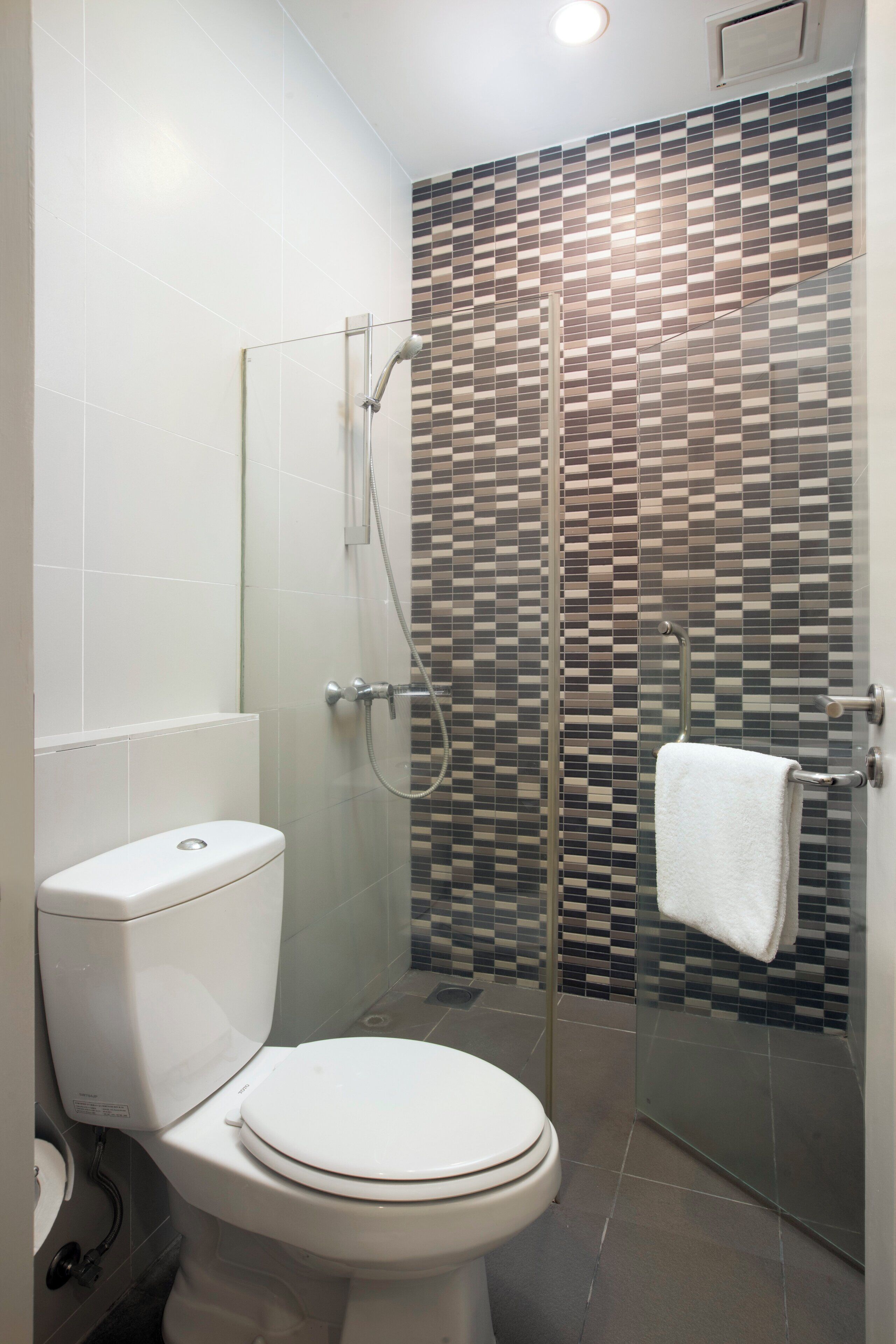 Une salle de bain moderne avec une douche à l’italienne en verre, des toilettes blanches et un mur recouvert de carreaux.