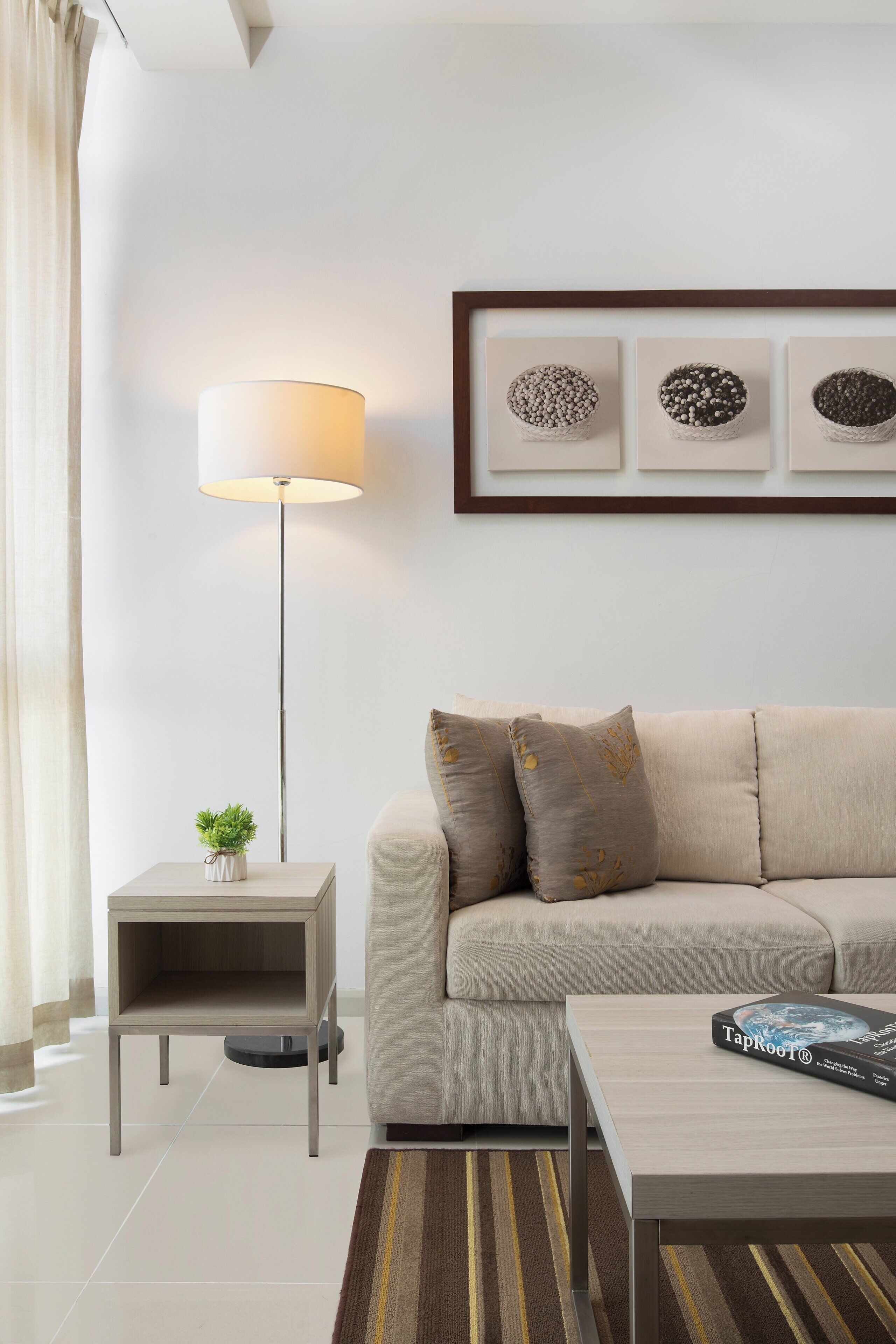 A modern living room with a sofa, a side table with a lamp, a coffee table, and framed artwork on the wall.