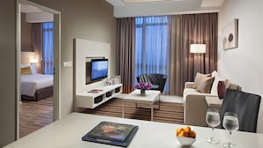 A modern hotel room with a bed, a TV, a sofa, a coffee table, and a dining table with a book and glasses. - Citadines Uplands Kuching (Kuching)