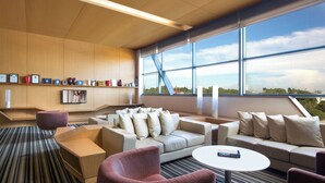 A modern hotel room with a large window, a sofa set, a coffee table, and a bookshelf with framed certificates. - Citadines Uplands Kuching (Kuching)