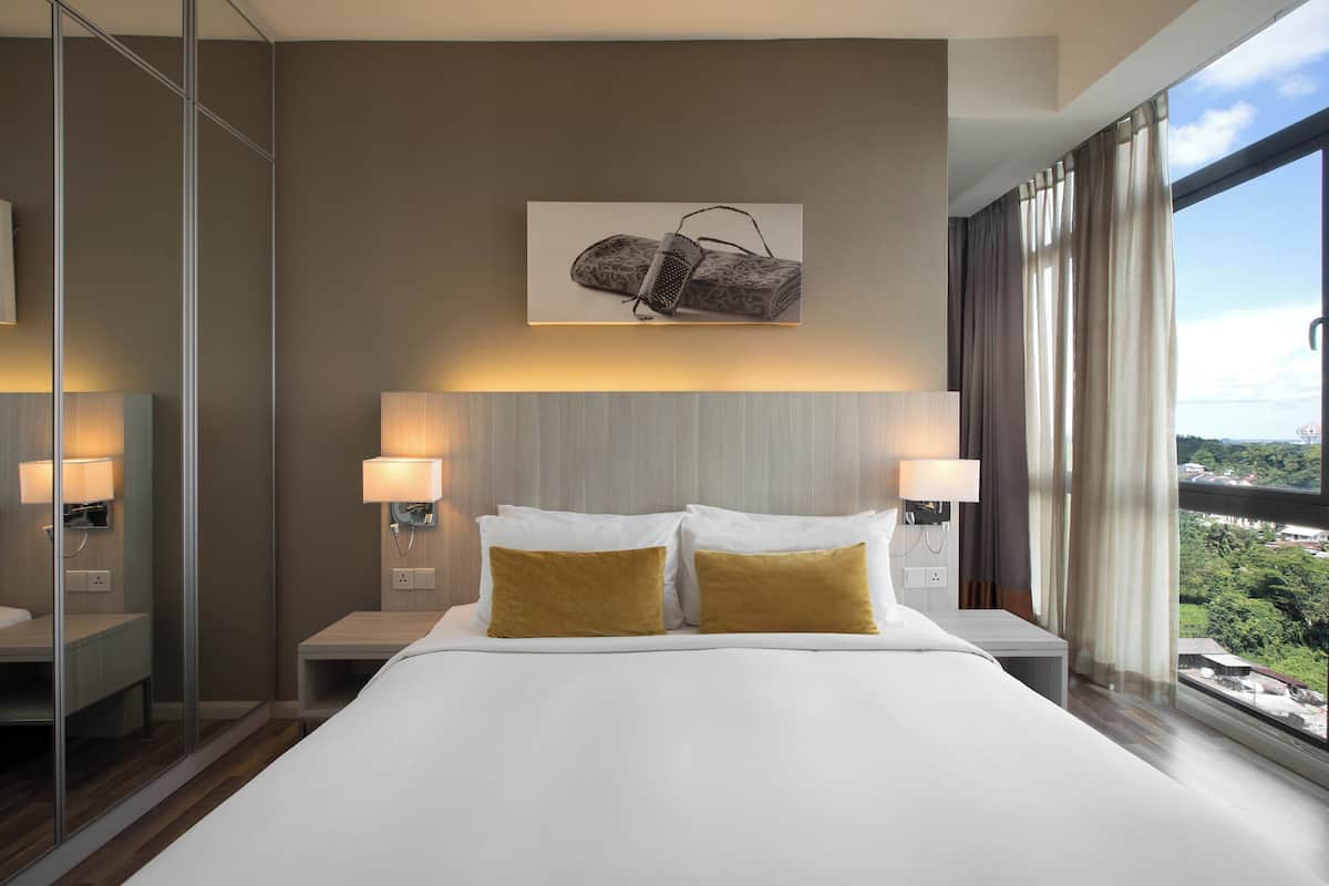 A modern hotel room with a large bed, two bedside lamps, a wall-mounted artwork, and a view of the city through large windows.