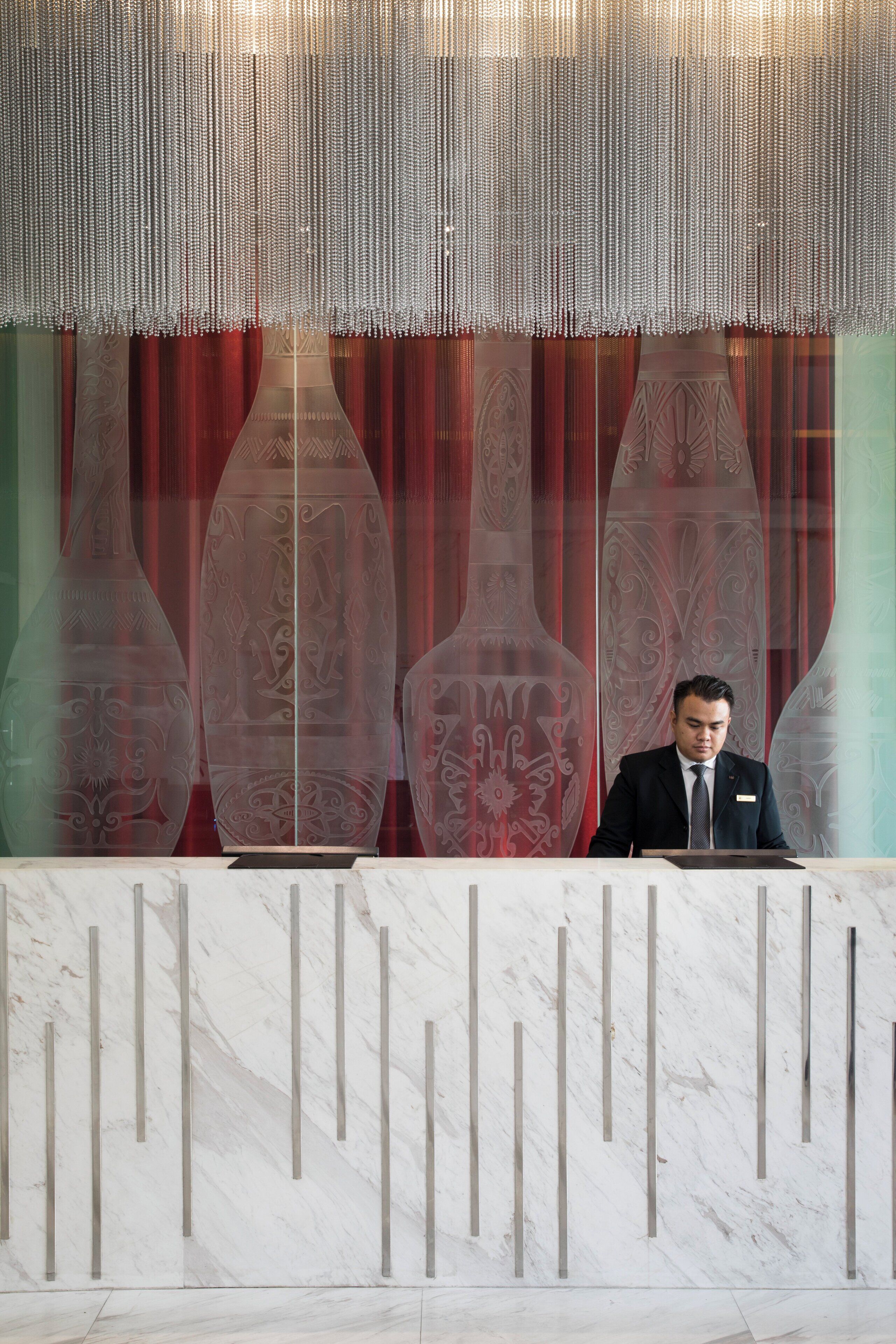 A reception desk with a marble surface and vertical metal supports. Behind the desk, there are large decorative glass panels with intricate designs.