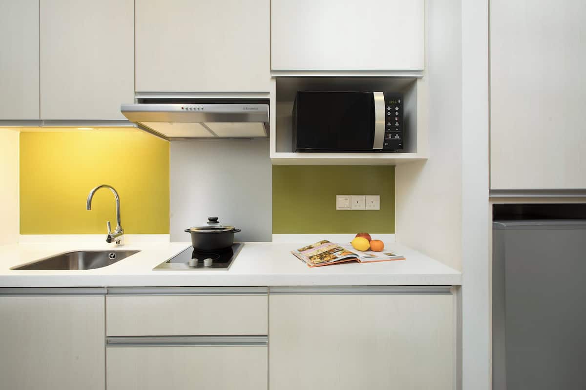 A modern kitchen with a stainless steel sink, a black stove, and a microwave on a white countertop.