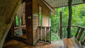 Une cabane en bois dotée d’un balcon, d’une terrasse en bois et offrant une vue sur une végétation luxuriante.