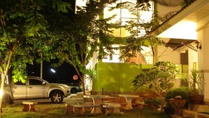 A courtyard with outdoor seating, a parked car, and a building with illuminated windows at night. - Green Home Resort (Surat Thani)