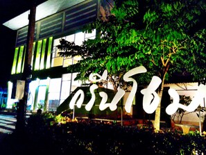 A building with a large illuminated sign, surrounded by greenery. - Green Home Resort (Surat Thani)