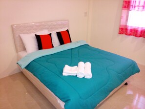 A bed with a teal bedspread, two pillows, and two rolled towels. - Green Home Resort (Surat Thani)