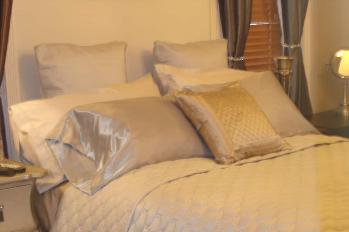 Uma cama bem arrumada com cobertura acolchoada, uma mesa de cabeceira com abajur e um quadro na parede.