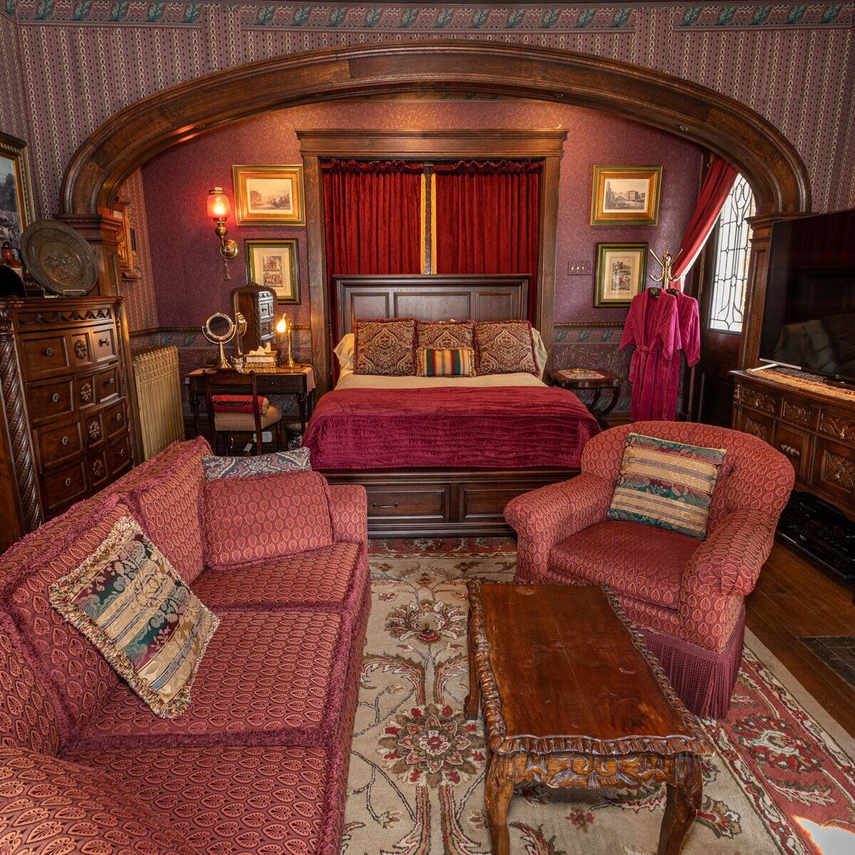 A room with a large bed, two armchairs, a wooden coffee table, and a dresser.