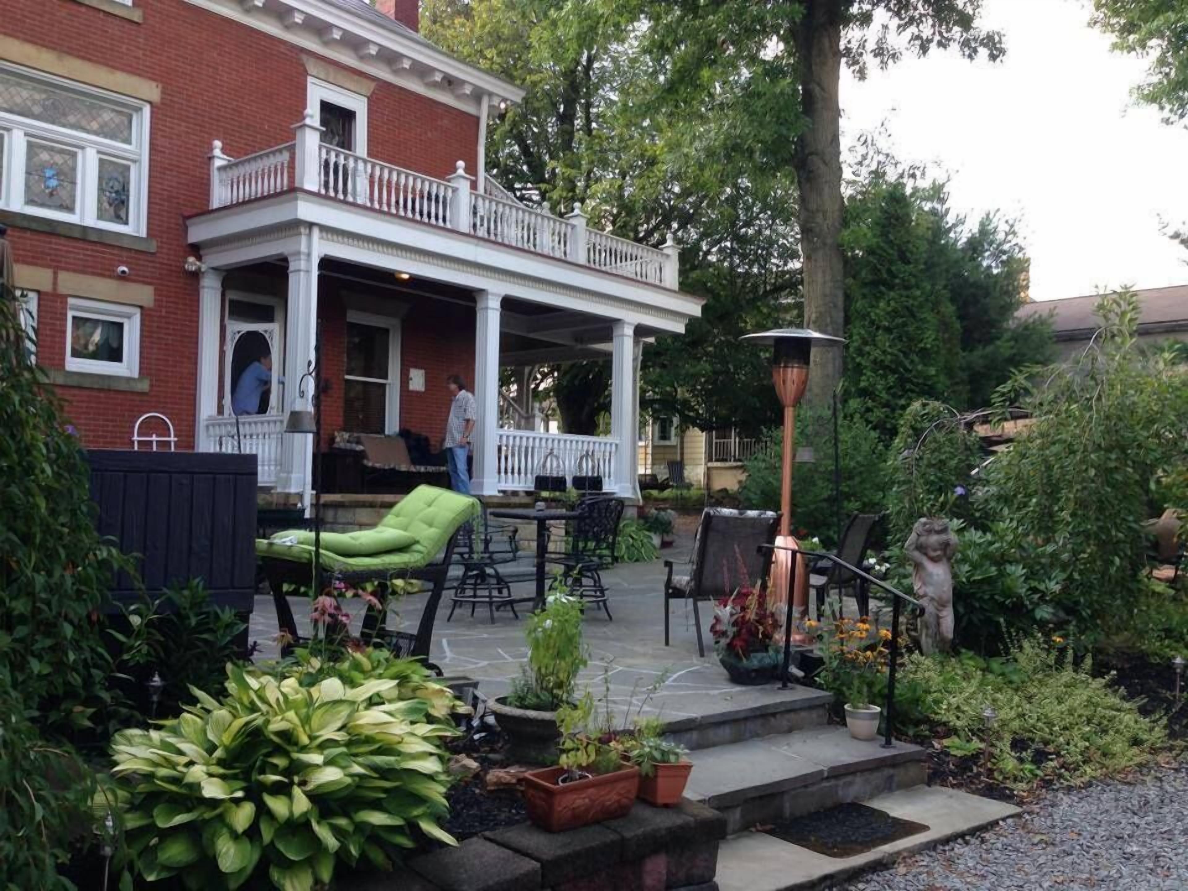 Eine überdachte Terrasse mit Gartenmöbeln, ein Ziegelhaus und ein Garten mit verschiedenen Pflanzen.