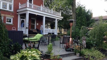 A covered patio with outdoor furniture, a brick house, and a garden with various plants.