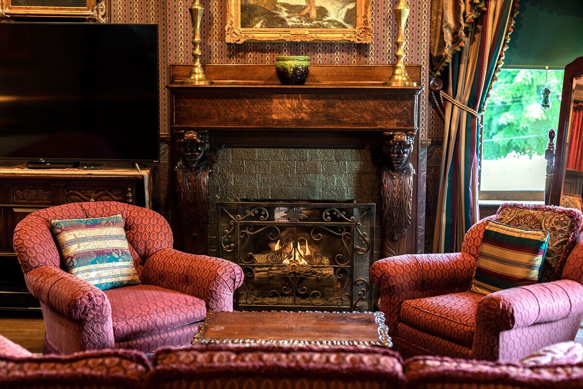 A traditional room with a fireplace, two patterned armchairs, a television, and a bookshelf.