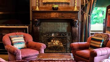 A traditional room with a fireplace, two patterned armchairs, a television, and a bookshelf.