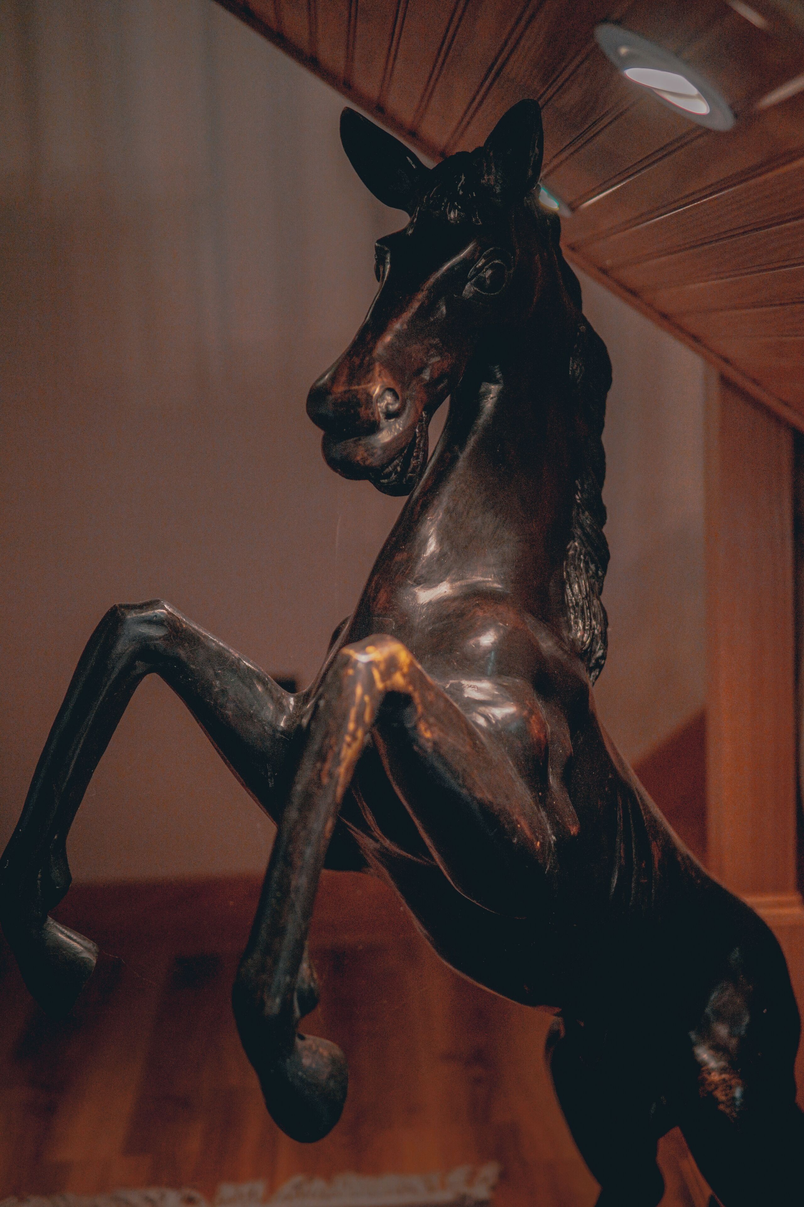 A wooden horse sculpture in a room with wooden paneling and a ceiling light.