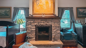 A cozy room with a stone fireplace, a large painting above it, and a bed with a wooden headboard.