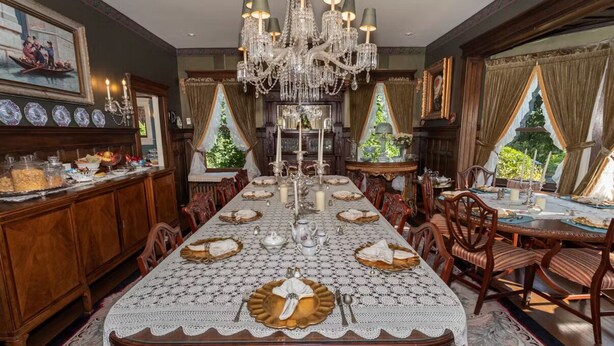 A formal dining room with a long table set for a meal, surrounded by wooden chairs.