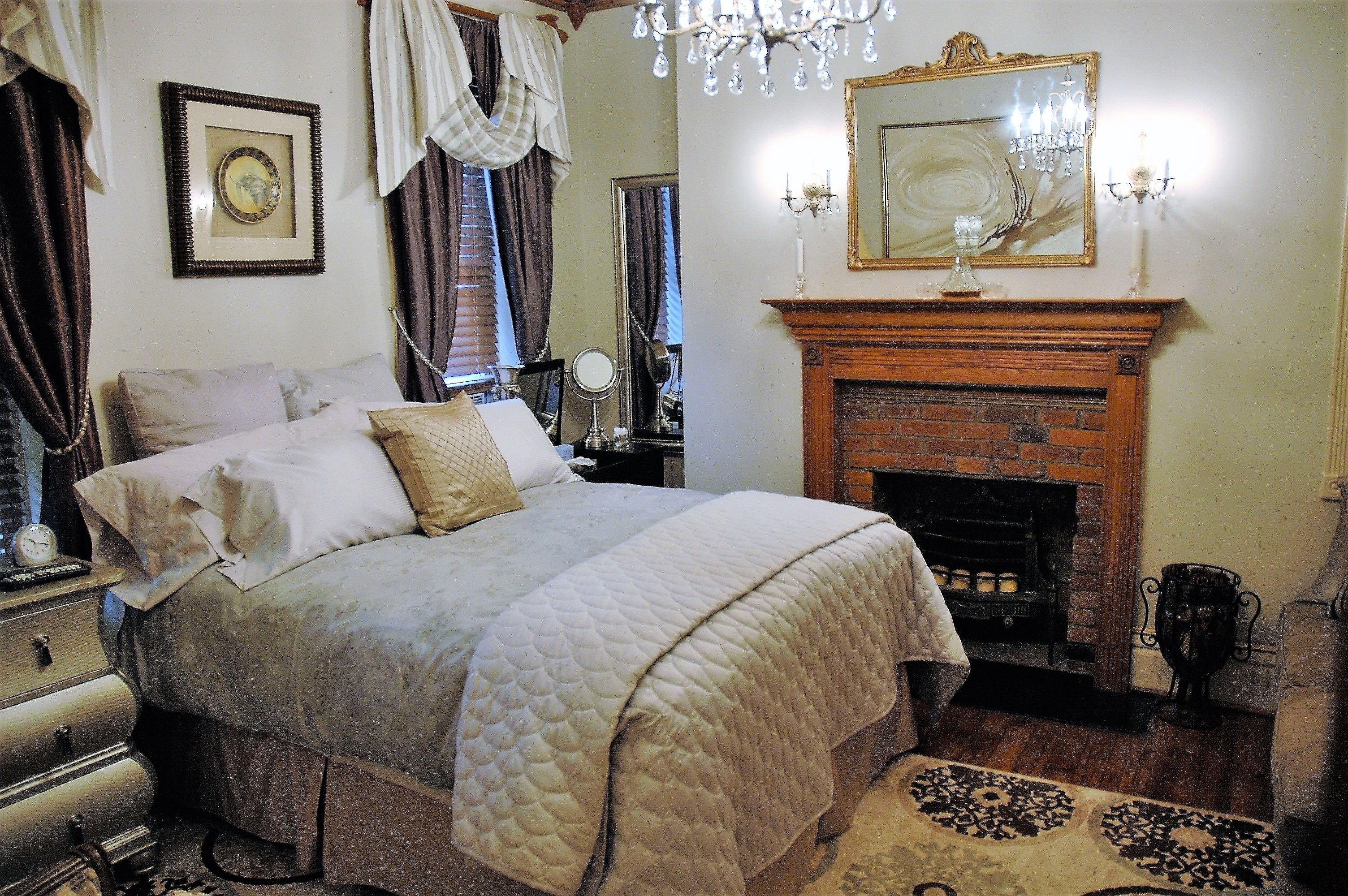 Un dormitorio con una cama grande, una chimenea, un candelabro y un espejo.