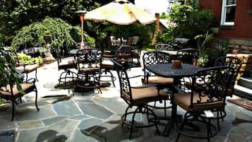 An outdoor patio with stone flooring, metal chairs, and a table with an umbrella.