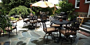 An outdoor patio with stone flooring, metal chairs, and a table with an umbrella. - South Broadway Manor (Scottdale)