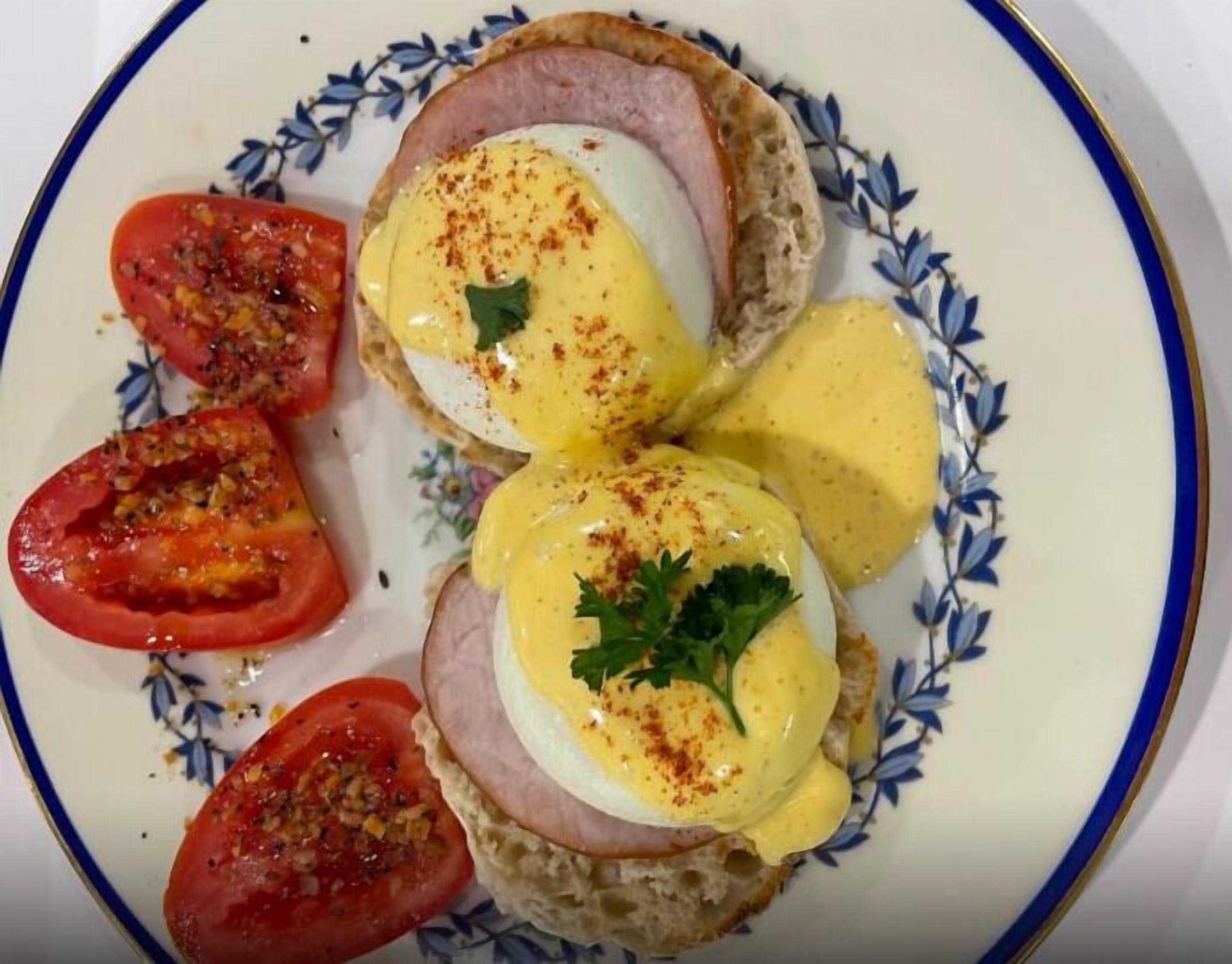 Une assiette contenant deux demi-sandwichs « œufs Bénédicte », des tranches de tomates et une garniture.