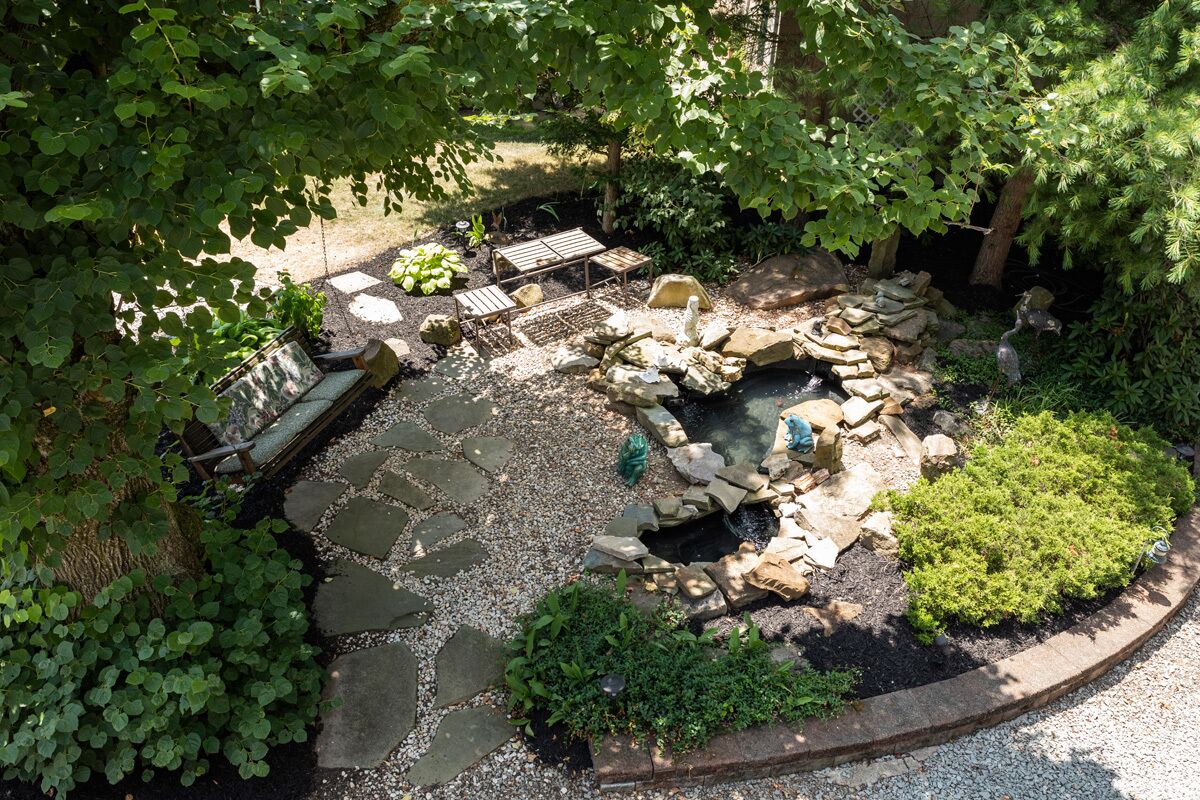 A garden with a stone fire pit, seating area, and a small pond.
