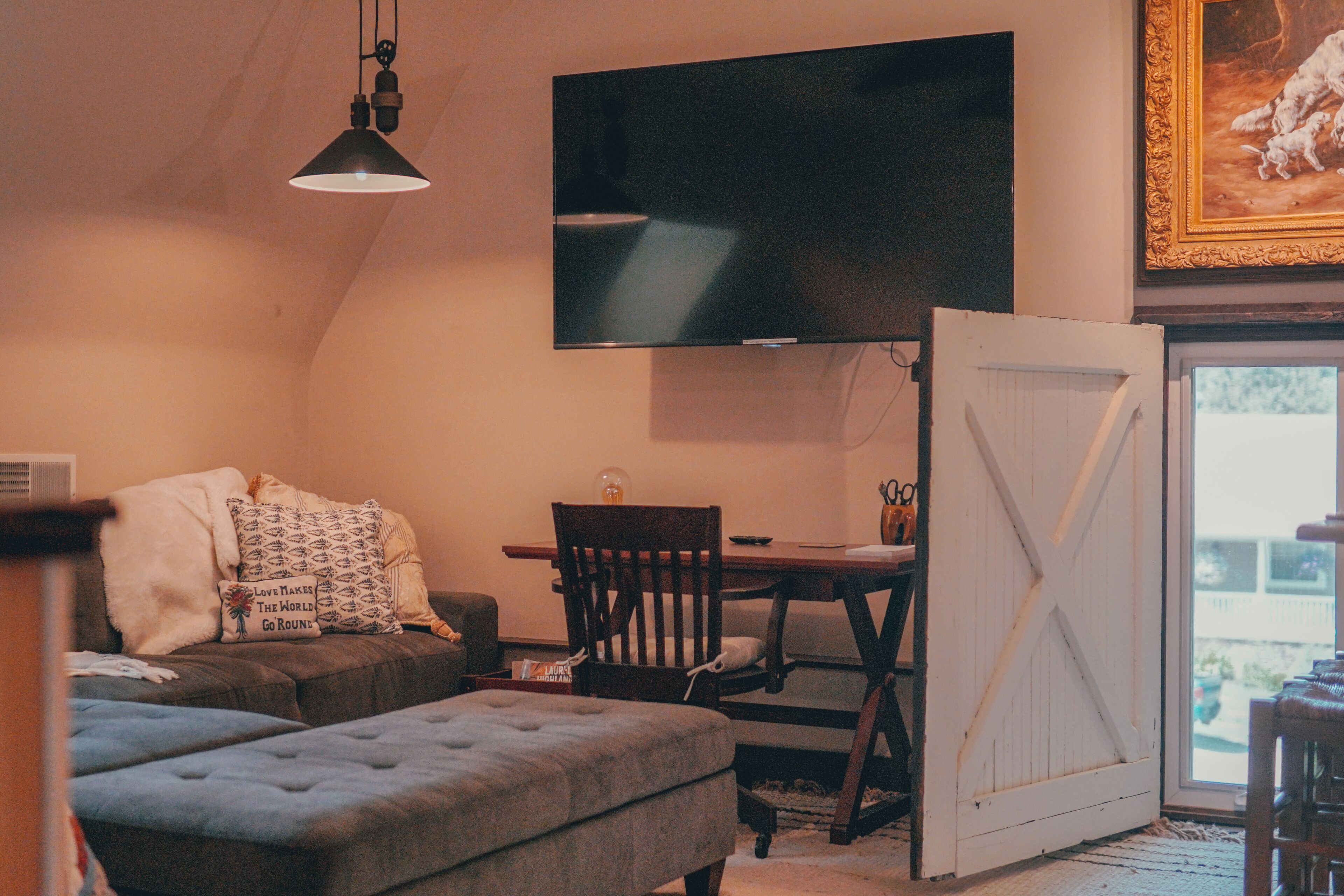 A cozy room with a flat-screen TV mounted on the wall, a dining table with chairs, a cushioned bench, and a large white door.