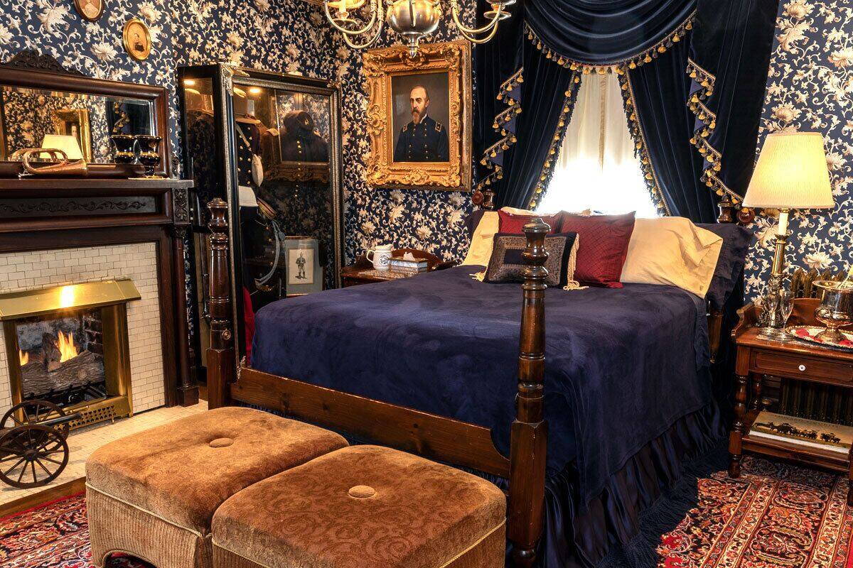 Quarto com uma cama grande, um candelabro, uma lareira e papel de parede ricamente decorado.