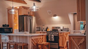 A kitchen with wooden cabinets, a stainless steel refrigerator, a stove, and bar stools.