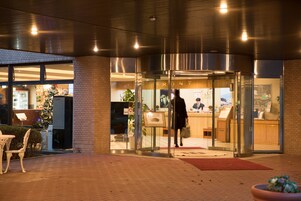 Entrada de hotel con puerta de cristal, mostrador de recepción y un árbol de Navidad en el exterior.