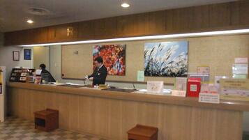 A reception area with a wooden counter, a check-in desk, and a check-out counter. There are two small wooden stools and a large painting on the wall.