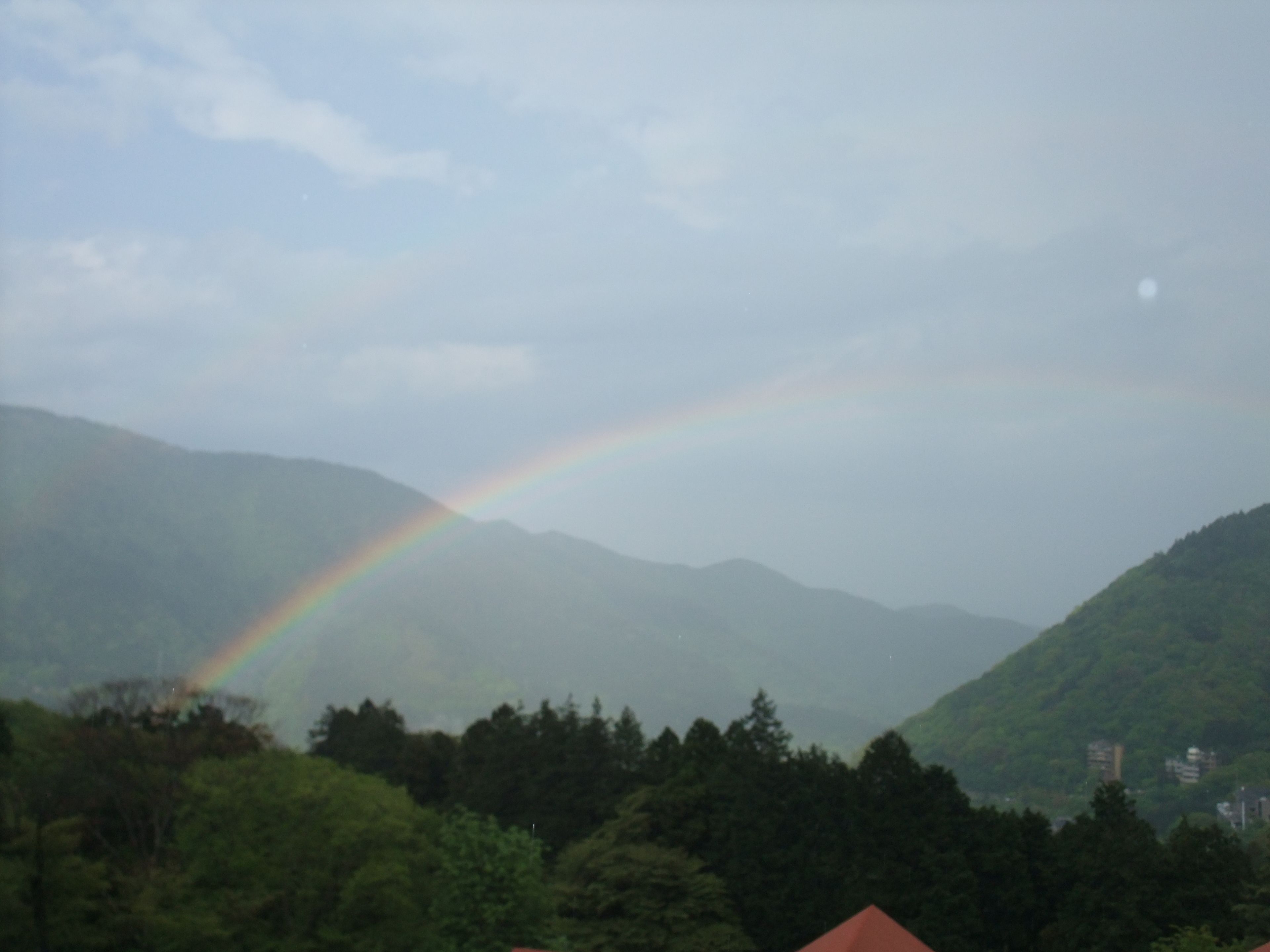 A mountain landscape with a rainbow and a red-roofed building in the foreground.