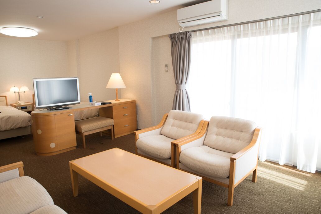 A hotel room with a TV, desk, two armchairs, a coffee table, and a bed.