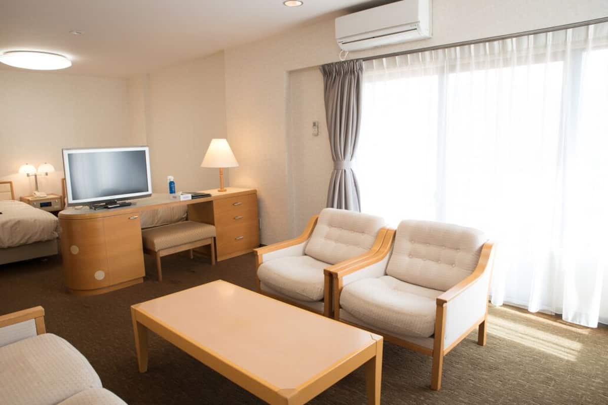 Une chambre d’hôtel équipée d’une télévision, d’un bureau, de deux fauteuils, d’une table basse et d’un lit.