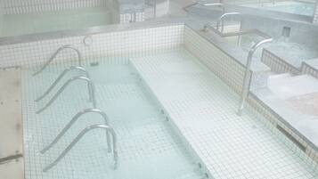 Piscina techada pública con paredes de azulejos, un reloj y barandales de metal.