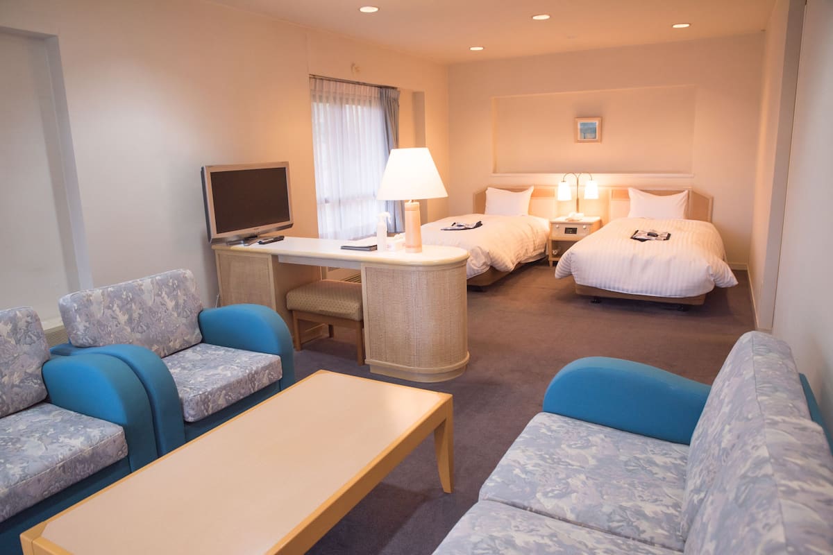 Une chambre d’hôtel équipée d’une télévision, de deux lits, d’un bureau avec une lampe et de deux canapés.