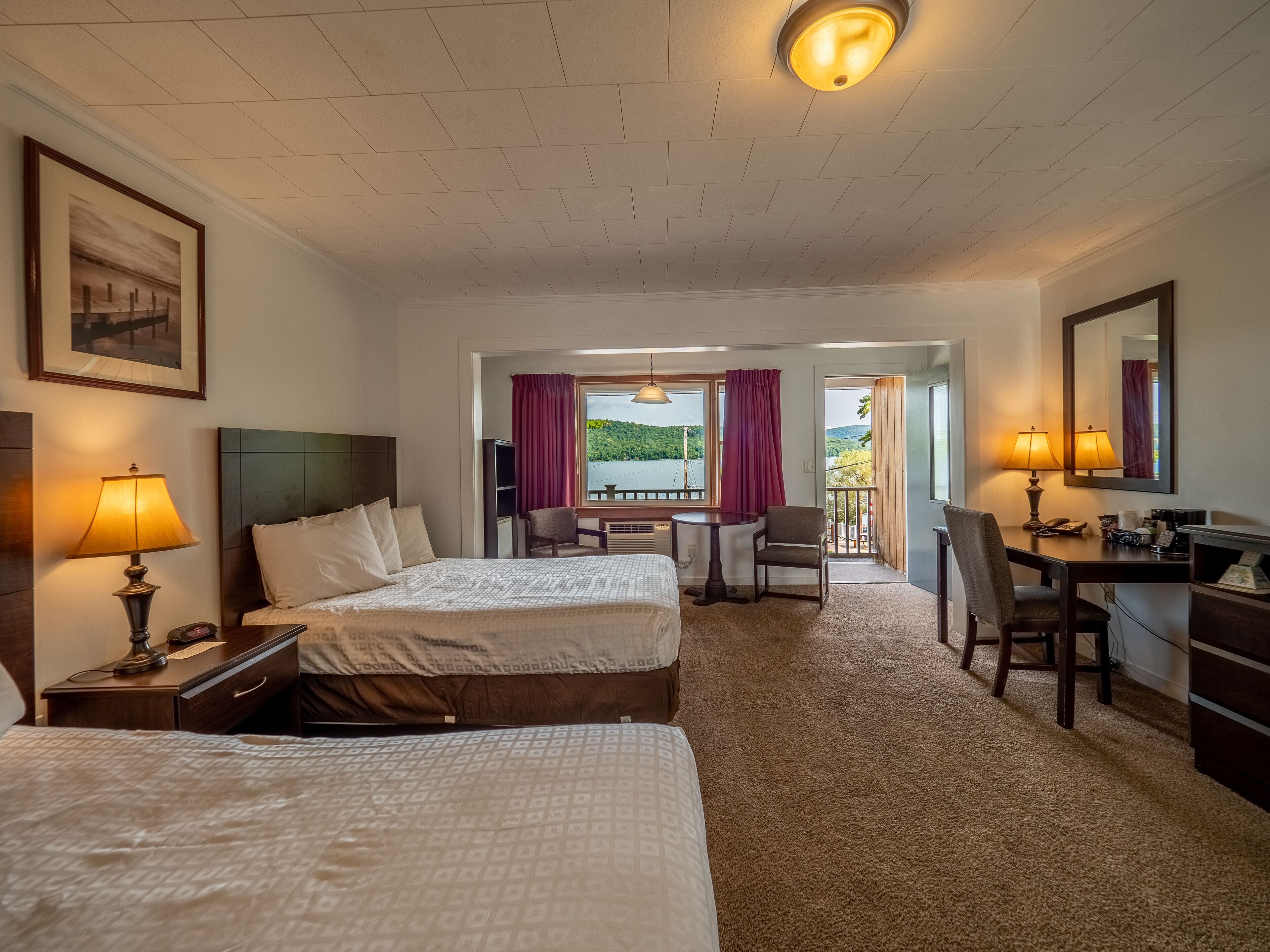 Ein Hotelzimmer mit zwei Betten, einem Schreibtisch, einem Stuhl, einer Lampe, einem Fernseher und Seeblick.