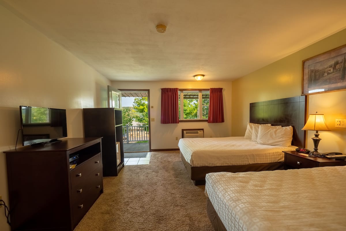 Ein Hotelzimmer mit zwei Betten, einem Fernseher, einem Schminktisch, einer Lampe und einem Fenster mit Vorhängen.