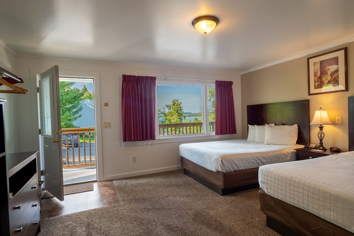 Ein Hotelzimmer mit zwei Betten, einem großen Fenster mit Vorhängen, einer Deckenleuchte und einem Bild an der Wand.