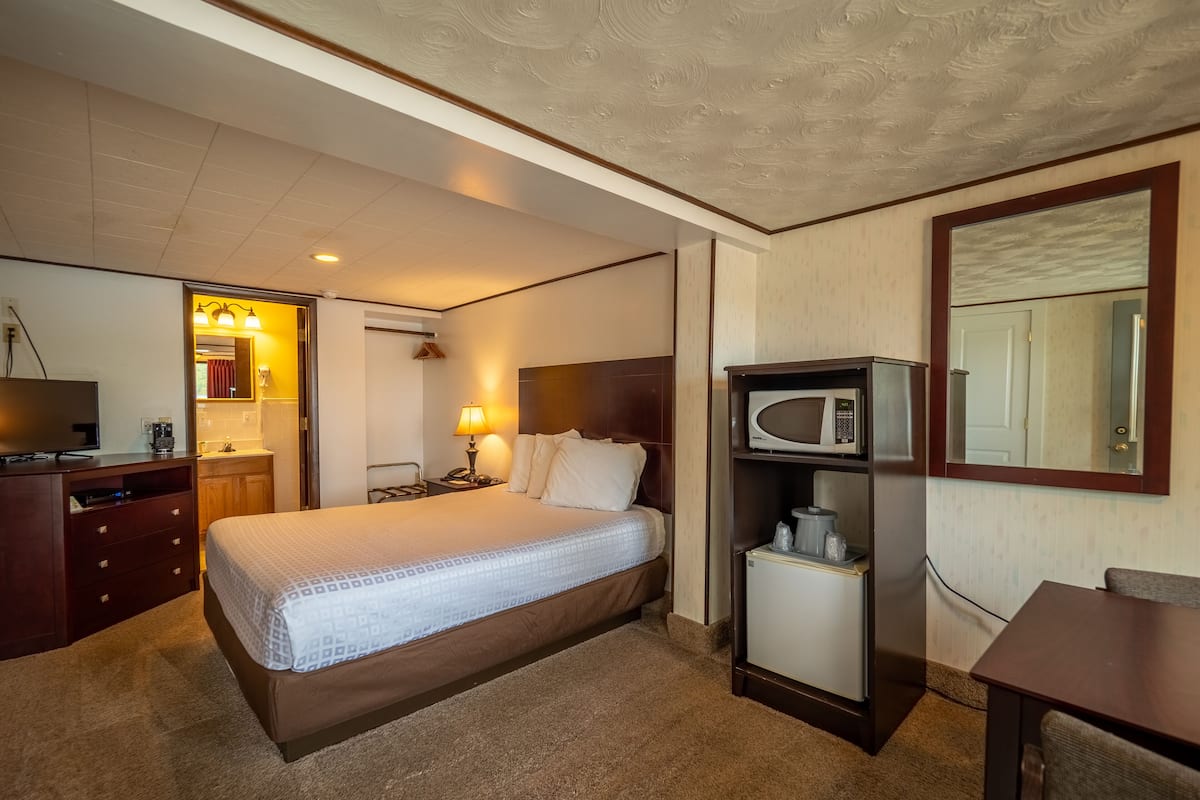 Ein Hotelzimmer mit Bett, Schreibtisch, Mikrowelle, Minibar und einem durchgegangenen Tür sichtbaren Badezimmer.