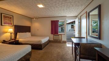 A hotel room with two beds, a desk, a chair, a lamp, and a window with a view of the outside.