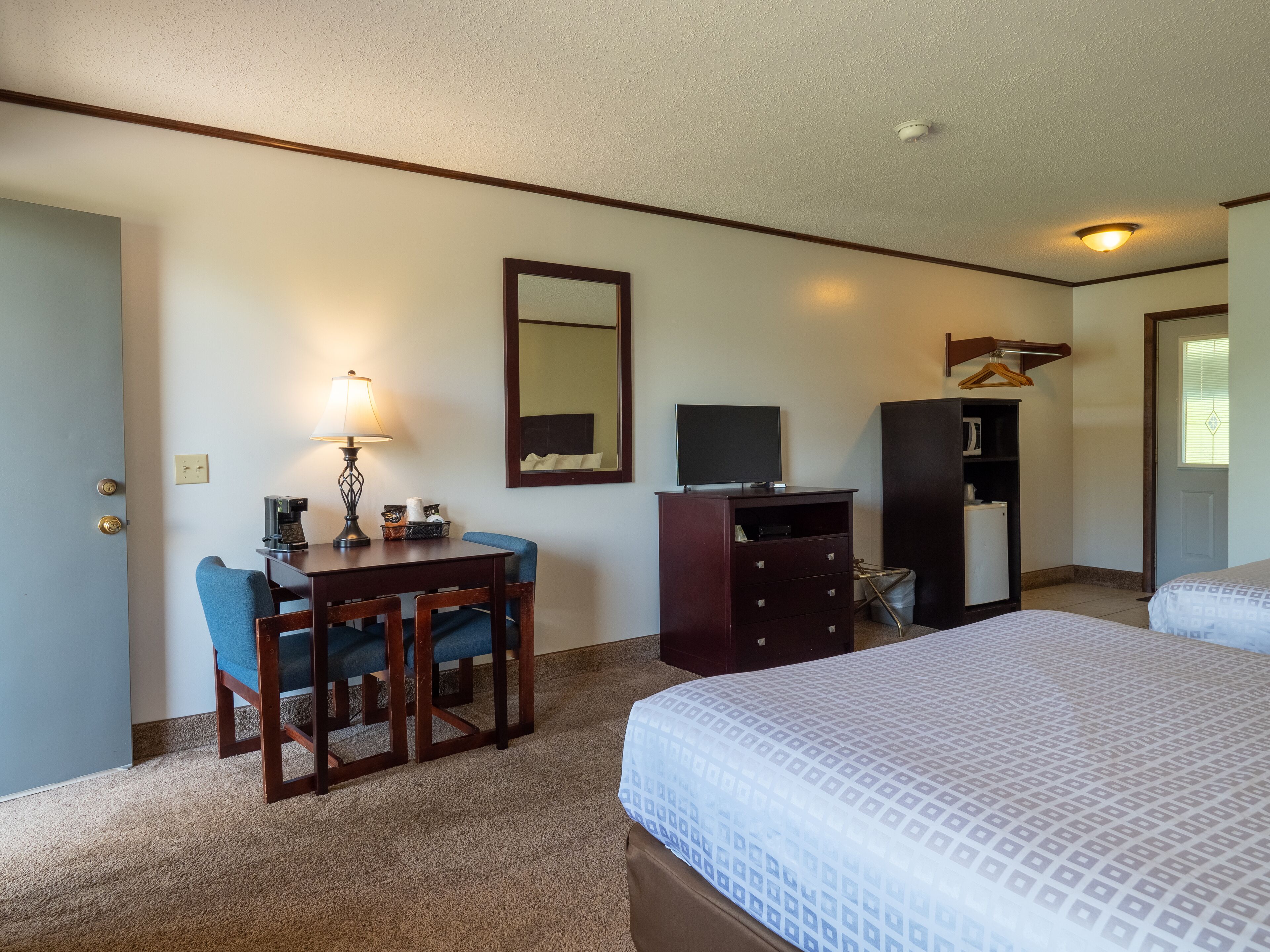 A hotel room with a bed, a desk with a chair, a dresser, a television, and a mirror.