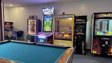 A pool table in a room with arcade games including 'Battlehead', 'Bull-o-Matic', and 'Hot Stuff'.