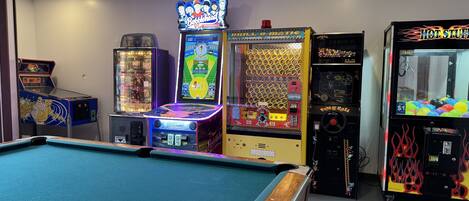 A pool table in a room with arcade games including 'Battlehead', 'Bull-o-Matic', and 'Hot Stuff'.