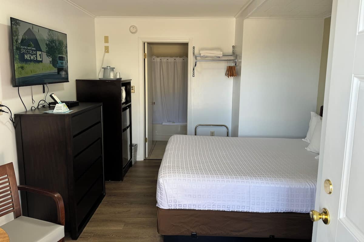 Ein Hotelzimmer mit einem Bett, einem Schreibtisch mit Computer, einem an der Wand montierten Fernseher und einer Tür zu einem Badezimmer.
