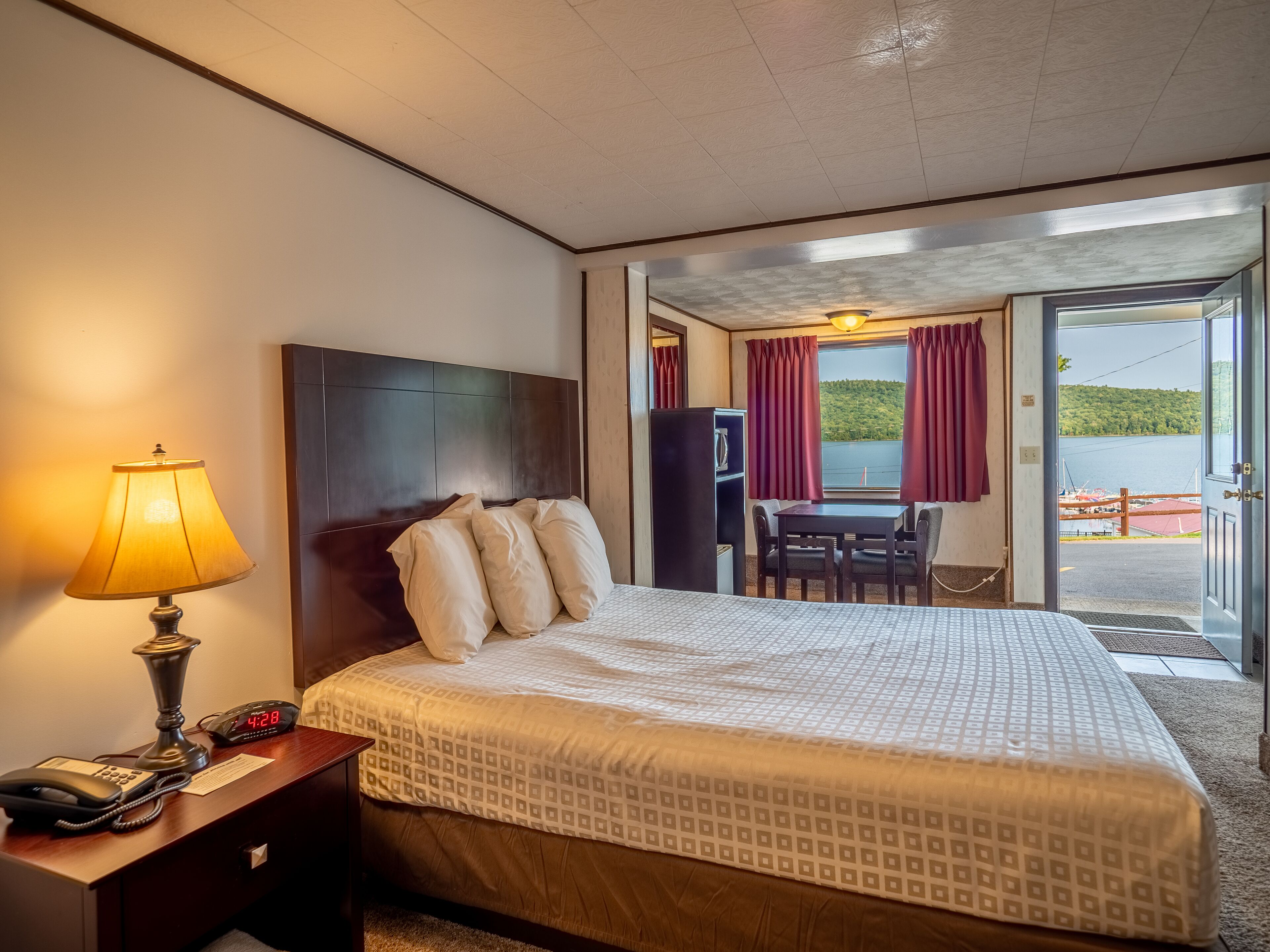 A hotel room with a bed, a desk with a lamp, a phone, and a view of the outdoors.
