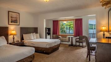 A hotel room with two beds, a desk, a chair, a window with a view of trees and water, and a ceiling light.