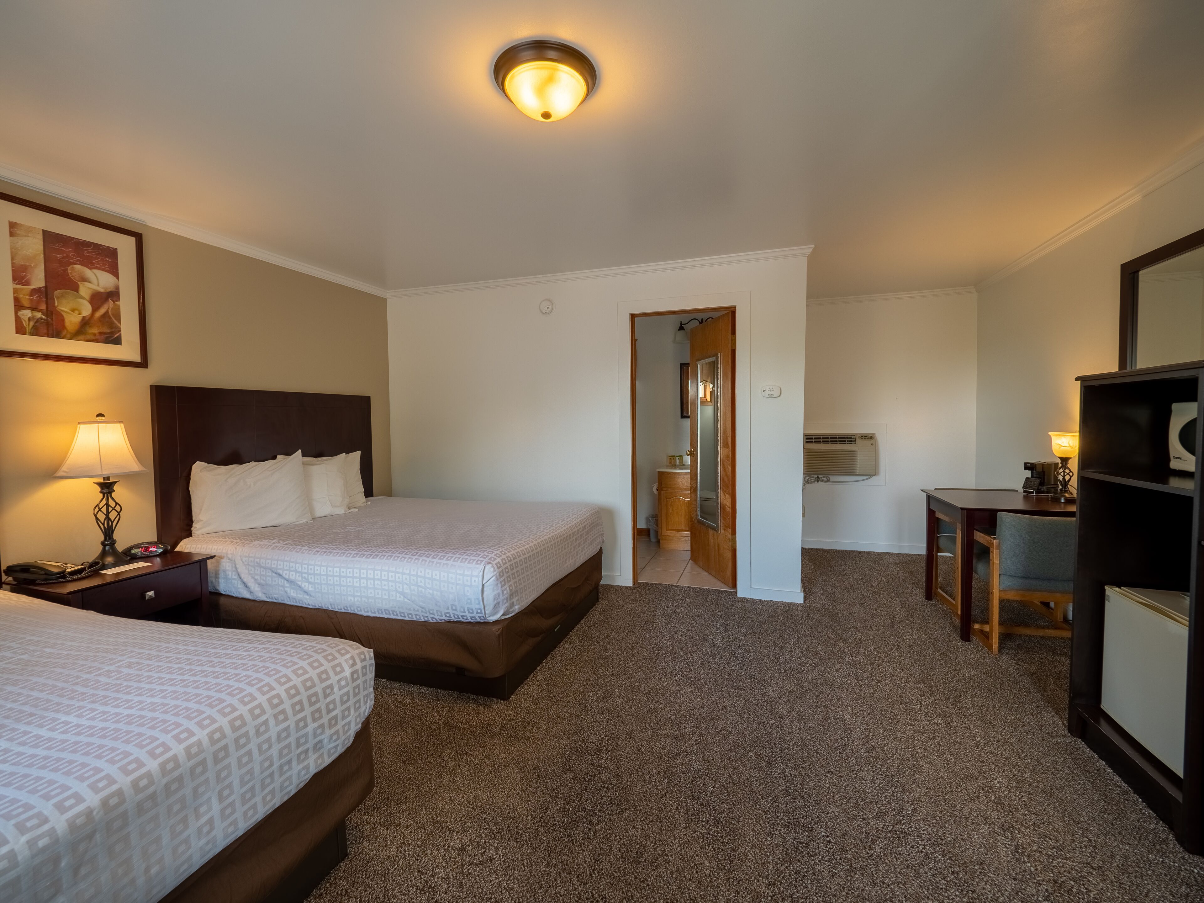 Une chambre d’hôtel avec deux lits, un bureau, une chaise, une lampe, un téléphone et un appareil de climatisation.