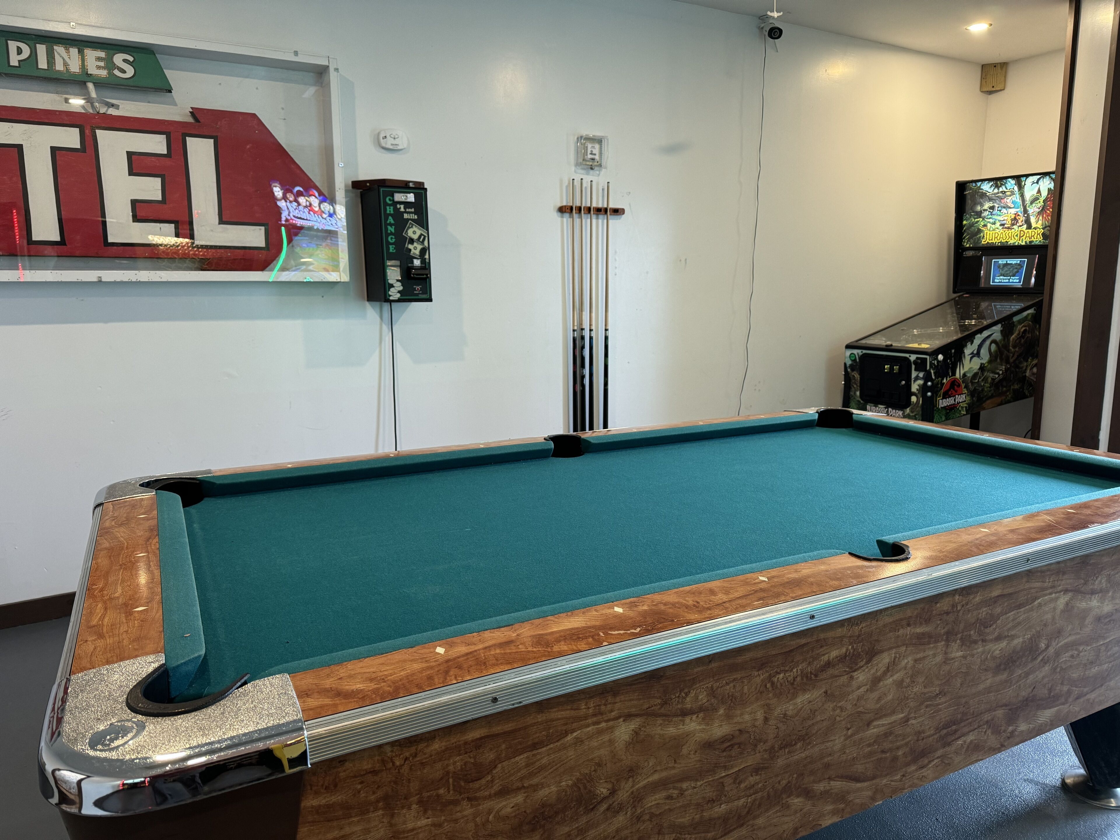 A pool table with a green felt surface, a wooden border, and a coin-operated change machine nearby.